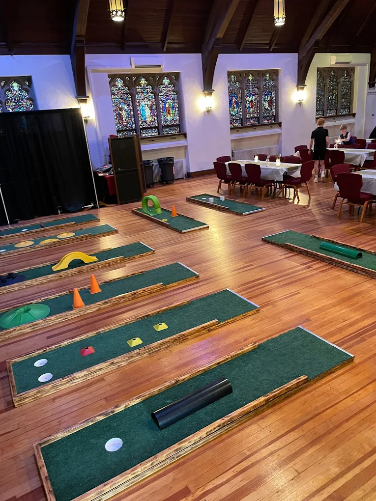 Portable mini golf course set up inside a historic hall with stained-glass windows